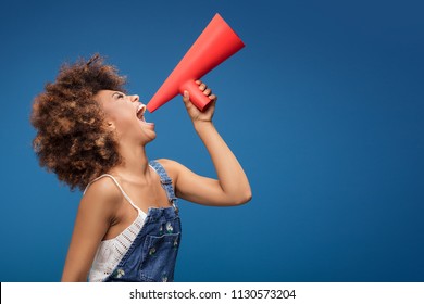 Smiling beautiful young African American woman with curly afro hair screaming by red megaphone. - Shutterstock ID 1130573204