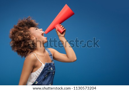 Smiling beautiful young African American woman with curly afro hair screaming by red megaphone.