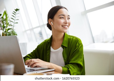 Smiling beautiful young asian woman working on laptop computer while sitting at the cafe indoors, looking through documents - Powered by Shutterstock