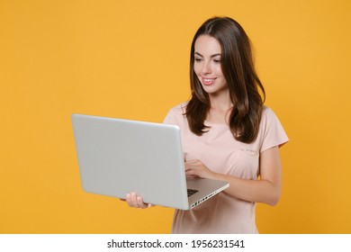 Smiling Beautiful Young Brunette Woman 20s Wearing Pastel Pink Casual T-shirt Posing Holding In Hands Working On Laptop Pc Computer Isolated On Bright Yellow Color Wall Background Studio Portrait