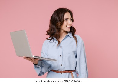 Smiling beautiful young brunette woman 20s wearing casual blue shirt dress posing standing working in laptop pc computer looking aside isolated on pastel pink colour background, studio portrait - Shutterstock ID 2070436595