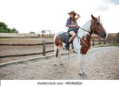 Smiling beautiful young woman cowgirl sitting and riding horse on ranch - Powered by Shutterstock
