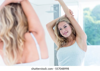 Smiling beautiful young woman looking at herself in the bathroom mirror at home