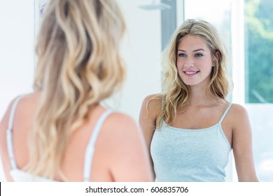 Smiling beautiful young woman looking at herself in the bathroom mirror at home