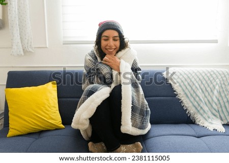 Smiling beautiful young woman looking happy and relaxed while wrapped in a blanket warming up on the couch while enjoying winter weather