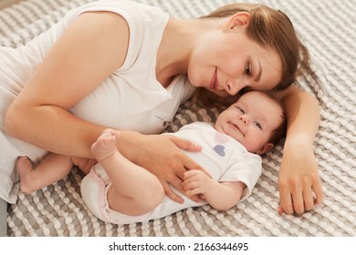 Smiling Beautiful Young Woman Lying On Bed And Playing With Her Cute Happy Baby