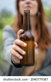 smiling beauty girl face to camera showing bottled beer. Close up with focus on the bottle blurred face. Natural background.