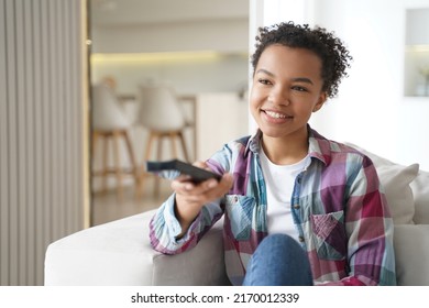 Smiling Biracial American Girl Holding Tv Controller, Switching Channels, Relax On Couch At Home, Happy Mixed Race Young Woman Spending Leisure Time With Television, Watching Movie Or Series.