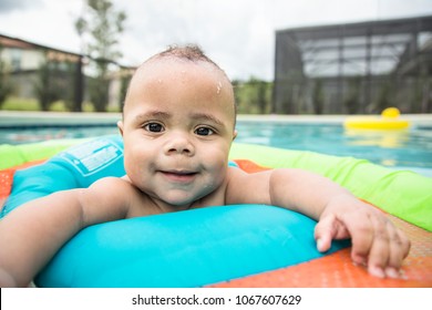 Smiling bi-racial baby boy playing in an outdoor swimming pool. A diverse child making an adorable expression
