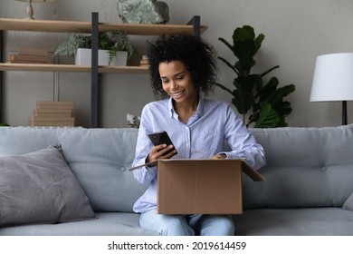 Smiling biracial female buyer client rate good delivery service or check shipment on cellphone. Happy African American woman shopping online on smartphone unpack open box with internet order. - Powered by Shutterstock