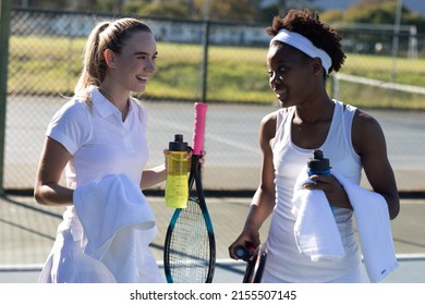 Smiling biracial female tennis players with bottles and towels talking during break at court. unaltered, sport, competition and tennis game concept. - Powered by Shutterstock