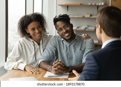 Smiling biracial man and woman talk with male real estate agent at office meeting. Happy African American young couple consult with realtor or broker, buy first shared house together. Rental concept.