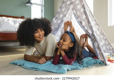 Smiling biracial mother with afro hair talking with daughter while lying in blanket tent at home. Camping, unaltered, family, togetherness, childhood, lifestyle and home concept. - Powered by Shutterstock