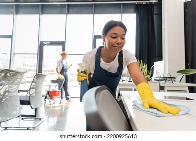 smiling bi-racial woman cleaning office desk with rag near colleague on blurred background - Shutterstock ID 2200925613