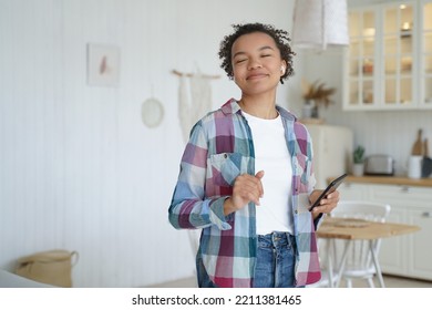 Smiling biracial young girl listens to music, enjoying sound, using musical apps on mobile phone at home. Modern biracial teen lady in wireless earphones, listening to songs, holding smartphone. - Powered by Shutterstock