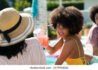 Smiling Biracial Young Woman With Afro Hair Toasting Cocktail With Friend While Enjoying Pool Party. Summer, Hangout, Drink, Unaltered, Friendship, Together, Social Gathering, Weekend Activities.