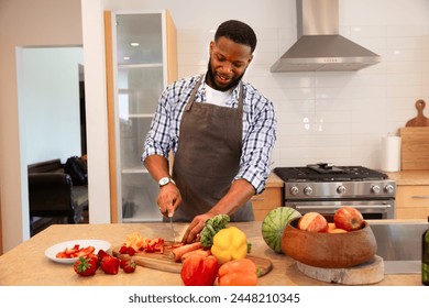 A smiling black African American is in his kitchen wearing apron preparing fruits and vegetable. Healthy meal, vegetarian meal - Powered by Shutterstock