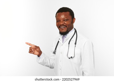 Smiling Black Bearded Doctor Man In White Coat With Stethoscope Points Finger To Left, Isolated On White Background. Adult Black African American Physician Therapist Portrait, Candid Male Emotion