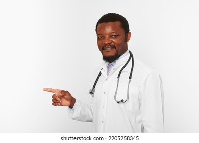 Smiling Black Bearded Doctor Man In White Coat With Stethoscope Points Finger To Left, Isolated On White Background. Adult Black African American Physician Therapist Portrait, Candid Male Emotion