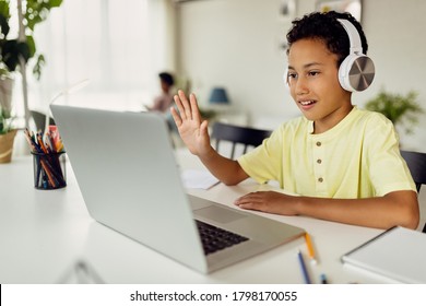 Smiling black boy making video call over laptop and waving while e-learning at home.  - Powered by Shutterstock