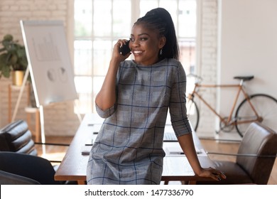 Smiling Black Businesswoman Manager Talking On Phone Making Business Call At Work, Happy Female African American Executive Having Mobile Conversation Consult Client By Mobile In Modern Office Space