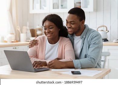 Smiling Black Couple With Laptop On Kitchen Calculating Bills At Home, Managing Family Finances Together, Young African American Spouses Paying Taxes Online Or Purchasing Grocery Delivery, Closeup