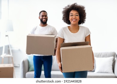 Smiling Black Couple On Moving Day Carrying Packed Cardboard Boxes Entering Into New Home. Real Estate And Apartment Ownership, Young Family Housing Concept. Selective Focus