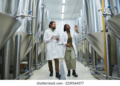 Smiling Black female brewer showing brewing equipment to inspector - Powered by Shutterstock