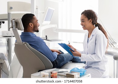 Smiling Black Female Dentist Filling Medical Chart, Talking To Patient In Dentist Chair, Clinic Interior