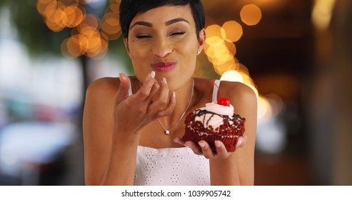 Smiling black female eating fancy cupcake in outdoor setting with bokeh lights - Powered by Shutterstock