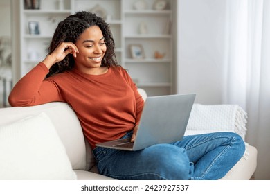 Smiling Black Female Relaxing With Laptop On Couch At Home, Happy Young African American Woman Sitting On Sofa In Living Room, Watching Movies Or Browsing Internet On Computer, Copy Space - Powered by Shutterstock