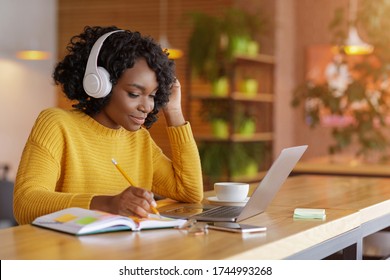 Smiling black girl with wireless headset studying online, using laptop at cafe, taking notes, copy space - Powered by Shutterstock