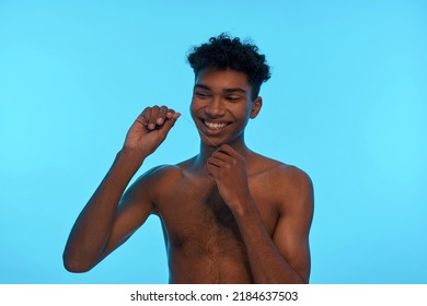 Smiling Black Guy Brushing His Teeth With Dental Floss. Young Slim Brunette Curly Man With Naked Torso. Dental Care And Hygiene. Isolated On Light Blue Background. Studio Shoot. Copy Space