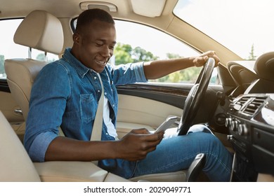 Smiling Black Guy Using Smartphone, Answering Messages Or Checking Emails While Driving Car, Side View, Copy Space, Sun Flare. Afro American Driver Checking His Cellphone, Dont Look At Road