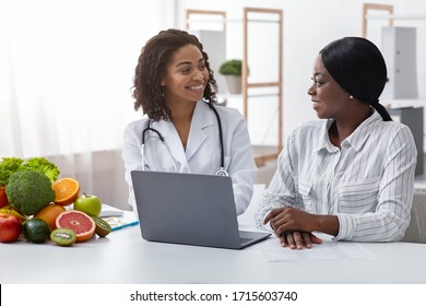 Smiling black lady doctor chatting with female patient at clinic, dietology and nutririon concept