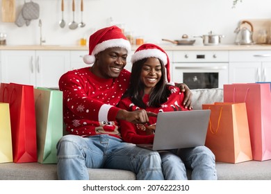 Smiling black lovers shopping online while staying home, happy millennial african american man and woman in Santa hats sitting on couch, using laptop, enjoying Christmas offers, copy space - Powered by Shutterstock