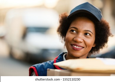 Smiling Black Mailwoman Making A Delivery In The City. 