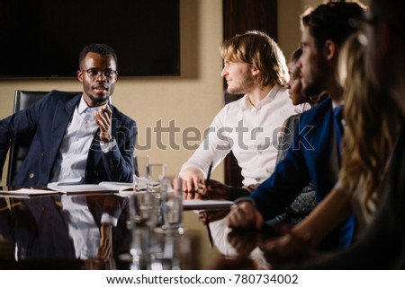 smiling black male boss talking to business team in conference room