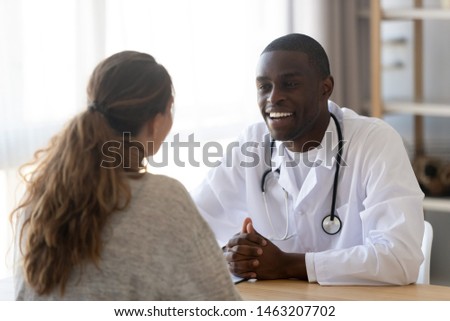 Smiling black male doctor listen female patient at medical meeting in clinic, happy african practitioner and woman client talking discuss health care good treatment result at checkup consultation