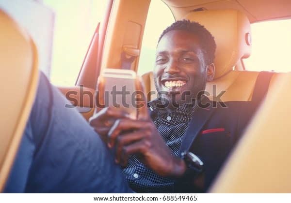 Smiling Black\
male using a smart phone in a\
car.