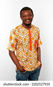 Smiling Black Man In Bright African Clothes Isolated On White Background, Casual African Wear. Happy Bearded Black Guy Portrait With Excited Funny Emotions, Pleasant Man With Hands In Jeans Pockets