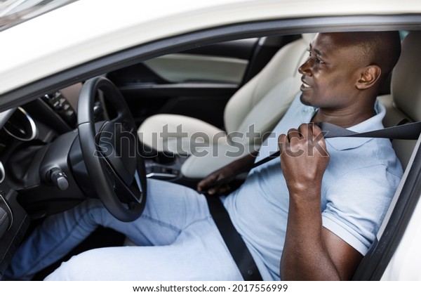 Smiling black man driver fasten seat belt, making\
test drive before purchasing new car, copy space. Excited african\
american guy going trip or vacation by brand new comfortable auto,\
side view