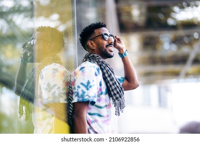 Smiling Black Man Leaning Against A Glass Wall Holding His Sunglasses