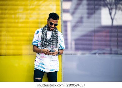 Smiling Black Man Leaning Against A Glass Wall Typing On His Smartphone