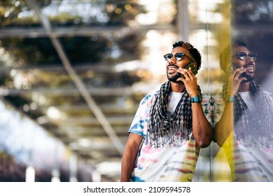 Smiling Black Man Leaning Against A Glass Wall Using His Smartphone