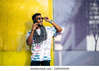 Smiling Black Man Leaning Against A Glass Wall Using His Smartphone