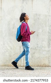 Smiling black man looking up while walking with mobile phone and backpack outdoors in city
