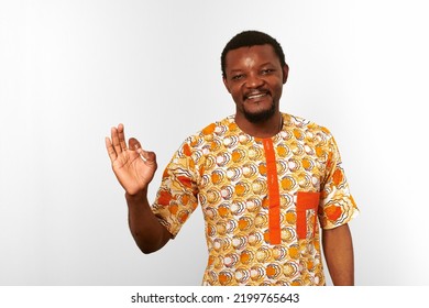 Smiling Black Man With OK Hand Gesture In African Bright Clothes Isolated On White Background, Casual African Wear. Nice Bearded Black Guy Portrait With Excited Funny Emotions