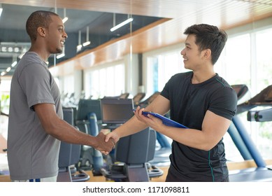 Smiling Black Man Thanking Personal Trainer In Gym. Young Guy Greeting Instructor With Gym Equipment In Background. Personal Trainer Concept.