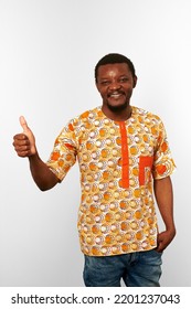 Smiling Black Man With Thumbs Up Hand Gesture In African Bright Clothes Isolated On White Background, Casual African Wear. Nice Bearded Black Guy Portrait With Excited Funny Emotions